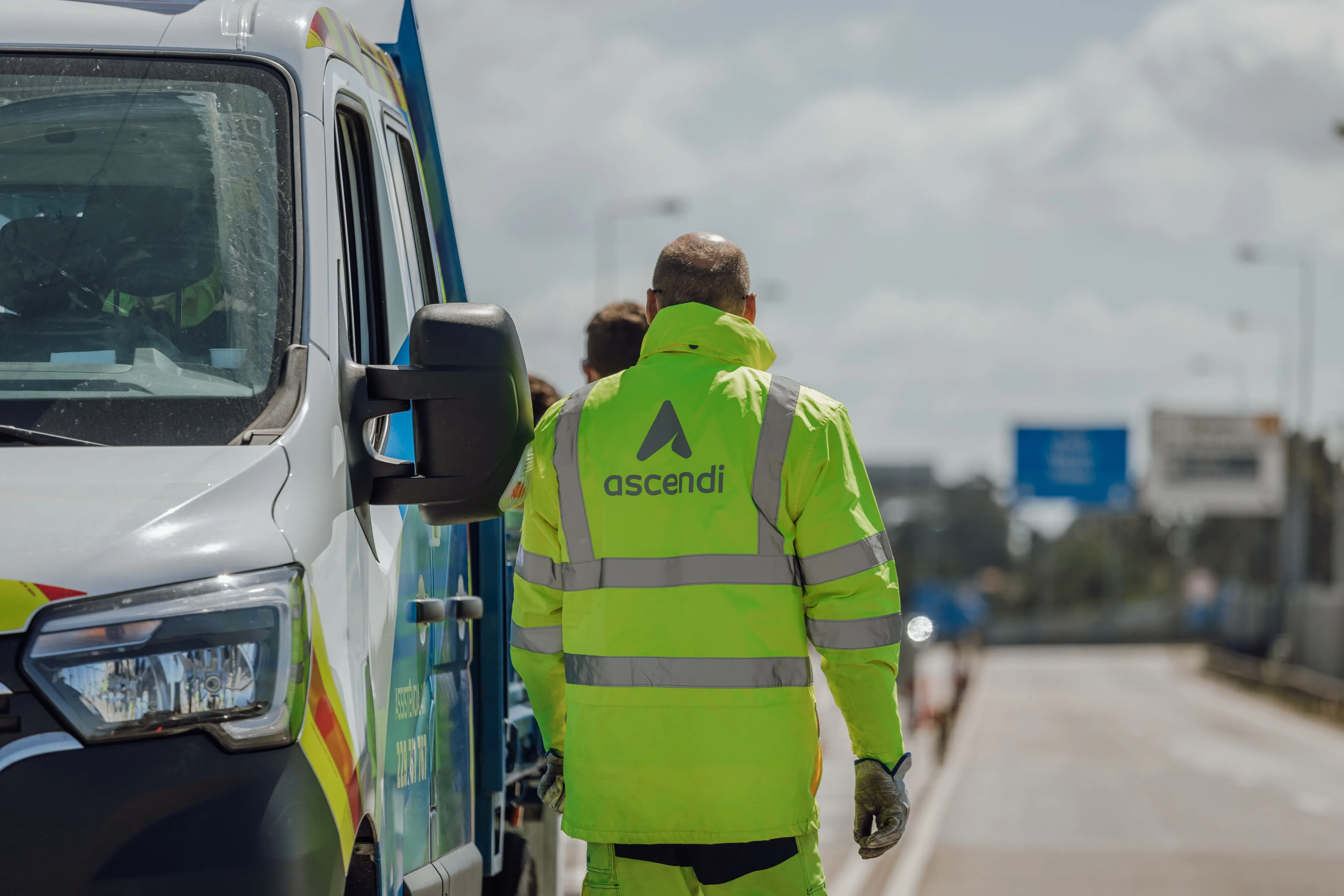 Colaborador da Ascendi com colete refletor junto a uma viatura de assistência na autoestrada.