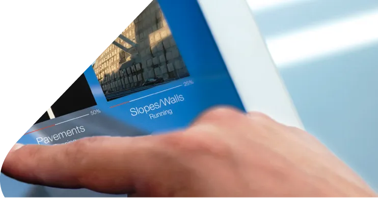 Mão a usar a plataforma SustIMS num tablet, com indicadores de pavimentos e taludes