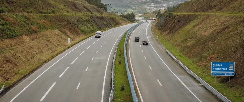 Motorway between green embankments, with a rumble strips sign