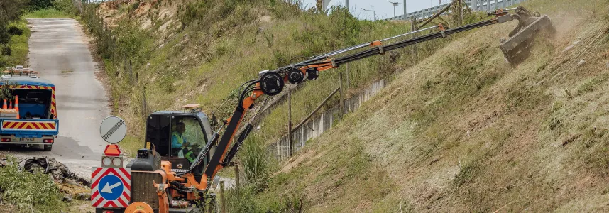Máquina com braço articulado a cortar a vegetação de um talude