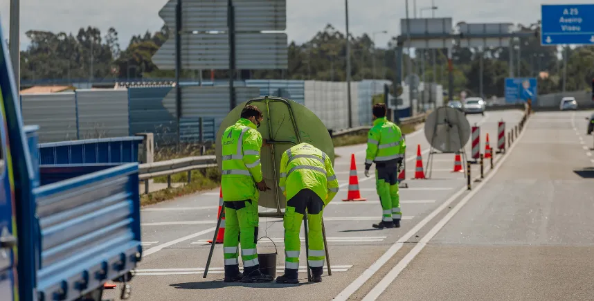 Equipa de manutenção com coletes refletores a trabalhar na berma de uma autoestrada sinalizada com cones