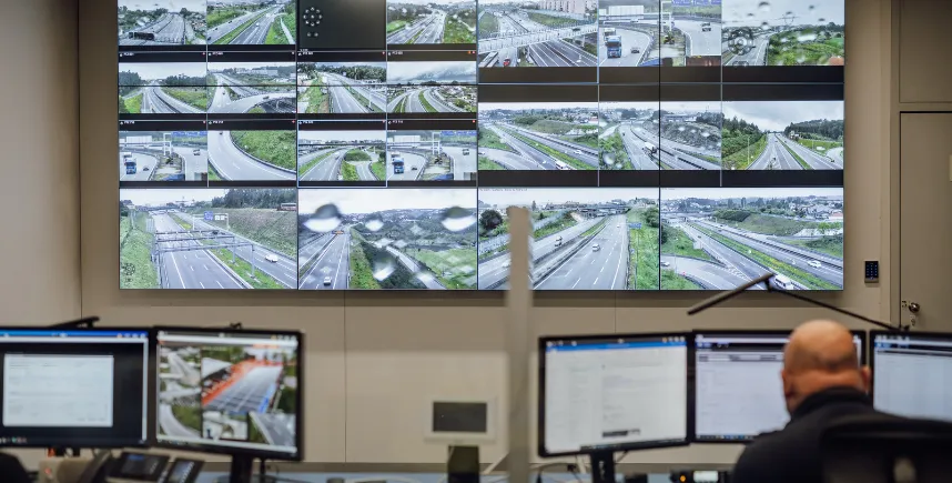 Operador num centro de controlo de tráfego, diante de uma parede de ecrãs com imagens das autoestradas