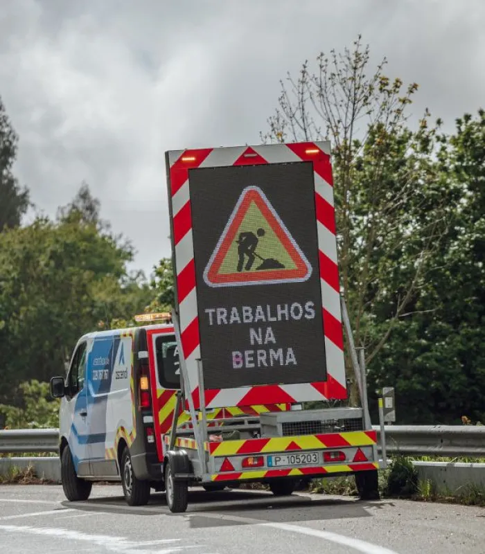 Carrinha de sinalização da Ascendi na berma de uma estrada, com um painel luminoso que indica «Trabalhos na berma».
